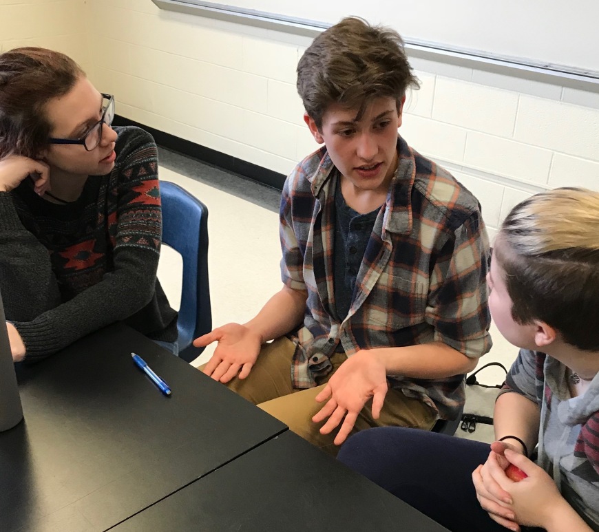 Three students are sitting at a table and having a conversation.