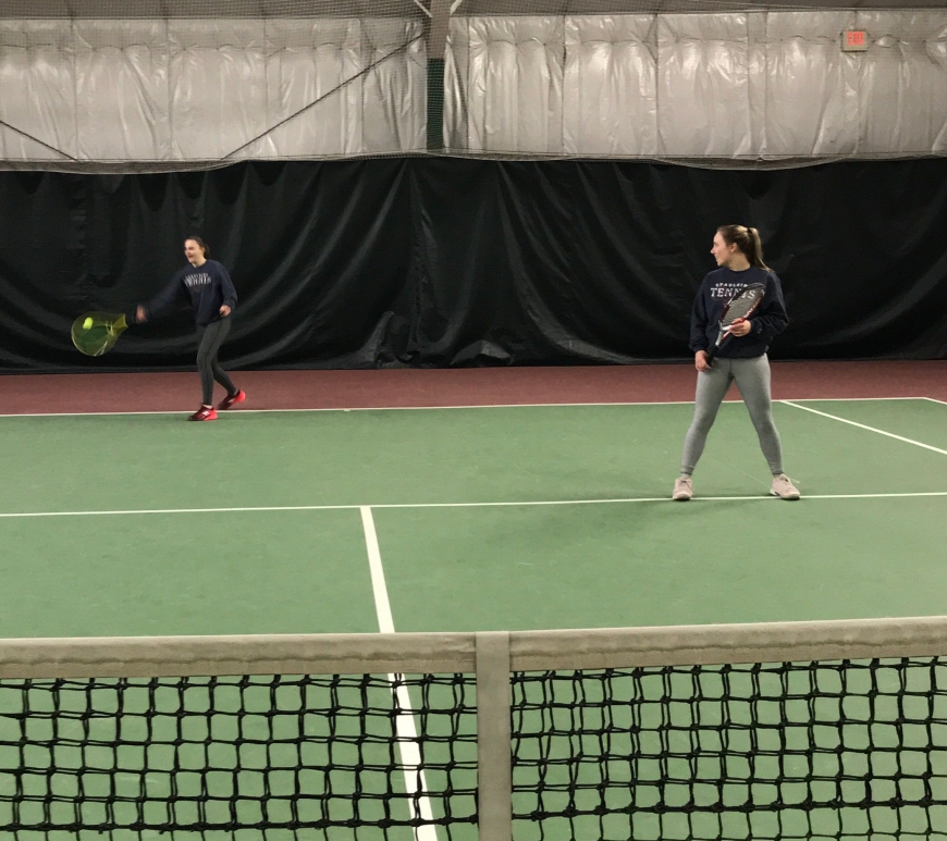 Two senior students practice tennis, with one returning the serve.